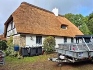 Sideparti af huset med nyt stråtag, kvistvindue og synlig stensokkel.